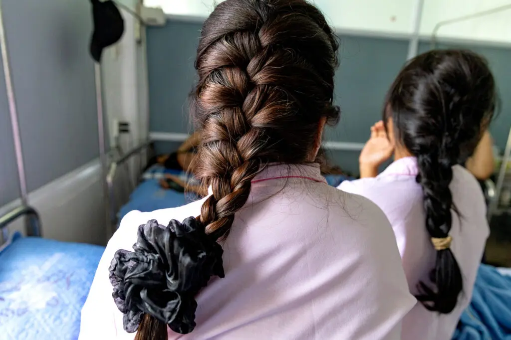 Two people seen from behind, both wearing pale pink tops and sporting long, dark braided hair, reflecting on their journey of breast reconstruction after cancer.