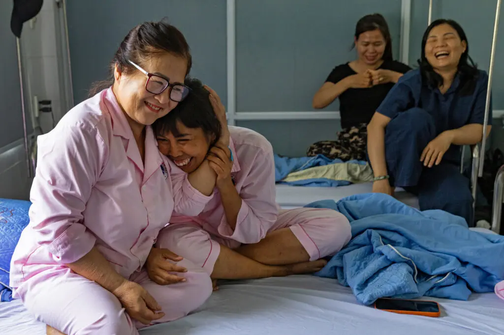 Four women laughing together while sitting on hospital beds after breast reconstruction.