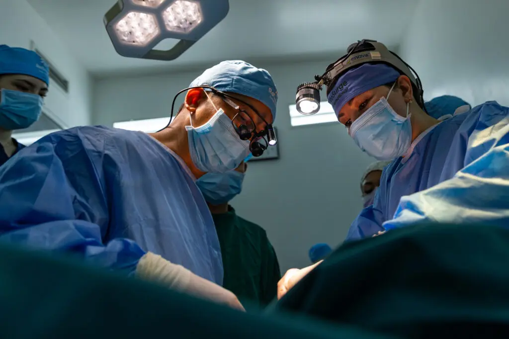 A team of surgeons in scrubs and face masks performs a surgery in an operating room as part of the healthcare community.