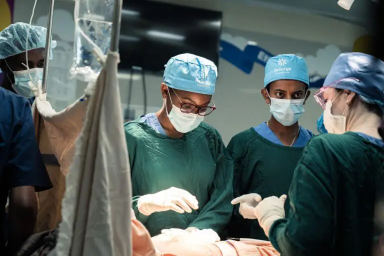 A surgical team in scrubs, masks, and caps performs breast cancer surgery in an operating room.
