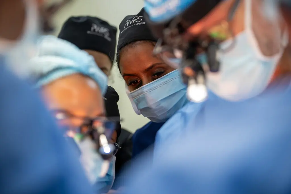 Pioneering Women in Reconstructive Surgery perform a medical procedure while wearing scrubs, caps, and face masks.