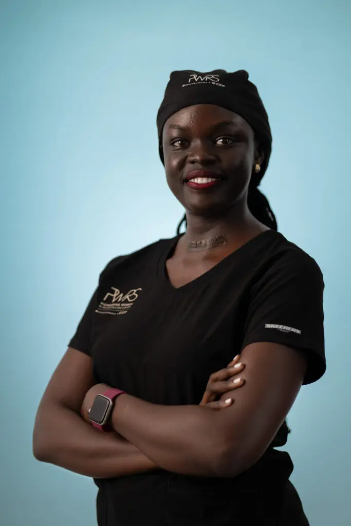 A smiling surgeon, one of the Pioneering Women in Reconstructive Surgery, wearing a black scrub top and surgical cap with their arms crossed.