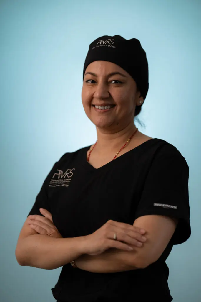 A smiling healthcare professional, one of the Pioneering Women in Reconstructive Surgery, wears a black scrub top and matching surgical cap with arms crossed.