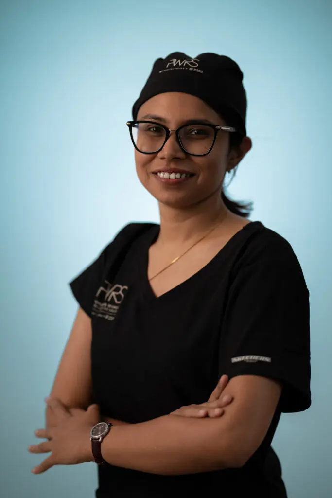 A woman in black medical scrubs, a scrub cap, and glasses stands with her arms crossed, representing Pioneering Women in Reconstructive Surgery.