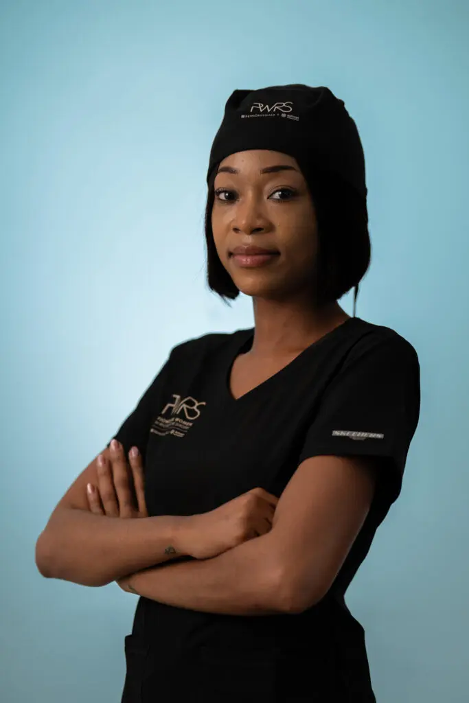 A Pioneering Woman in Reconstructive Surgery wears a black scrub top and surgical cap with her arms crossed against a light blue background.