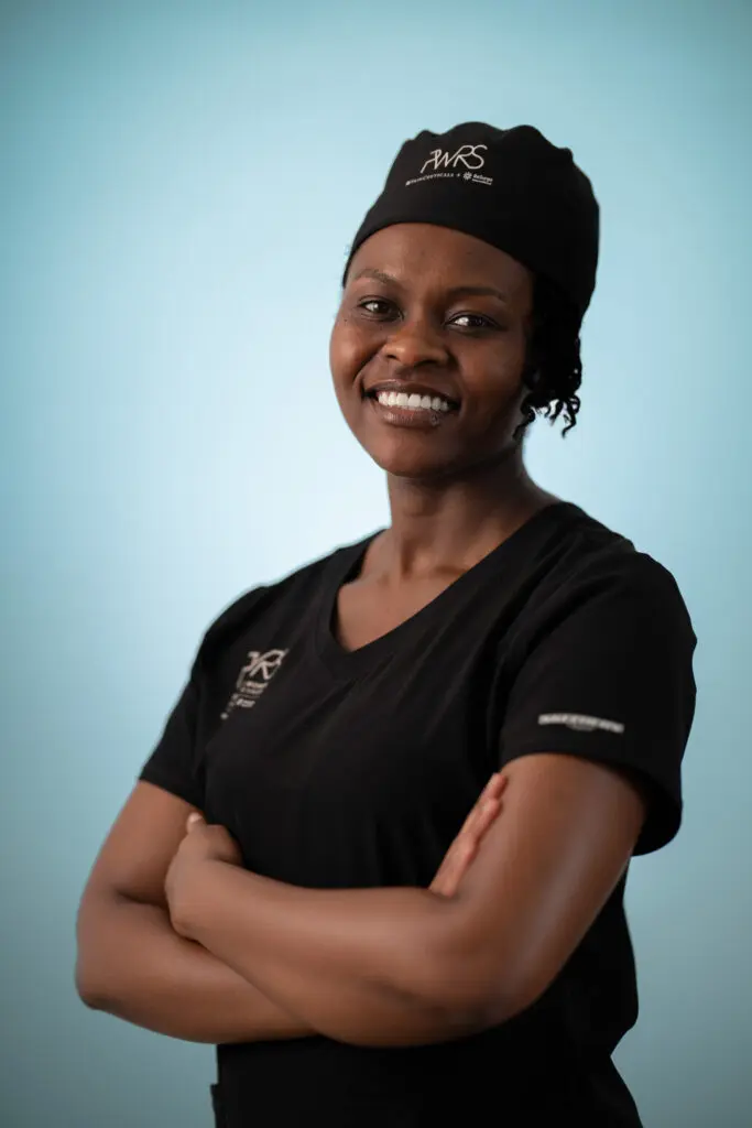 A smiling healthcare worker in black scrubs and a scrub cap representing Pioneering Women in Reconstructive Surgery with arms crossed.