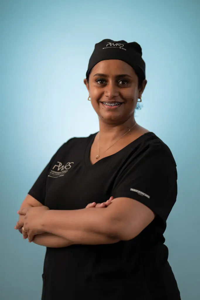 A smiling healthcare professional and Pioneering Women in Reconstructive Surgery member wearing a black scrub top and matching surgical cap with their arms crossed.