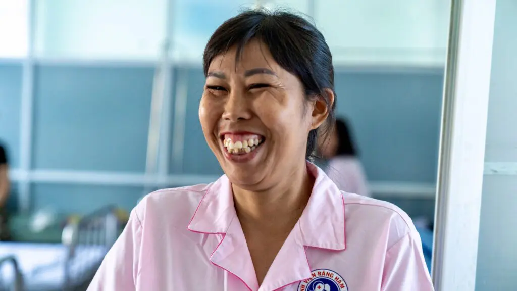 A woman wearing a pink hospital uniform smiling broadly as part of a supportive hospital community.