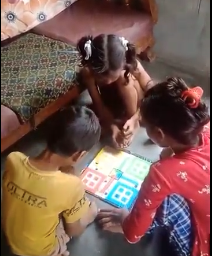 Three children sit on the floor playing a Ludo board game.
