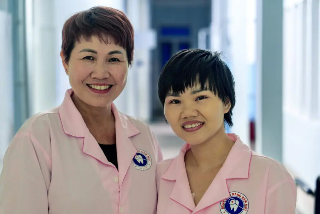 Two dental professionals in pink uniforms stand side-by-side smiling at a New York ballroom event for survivors.