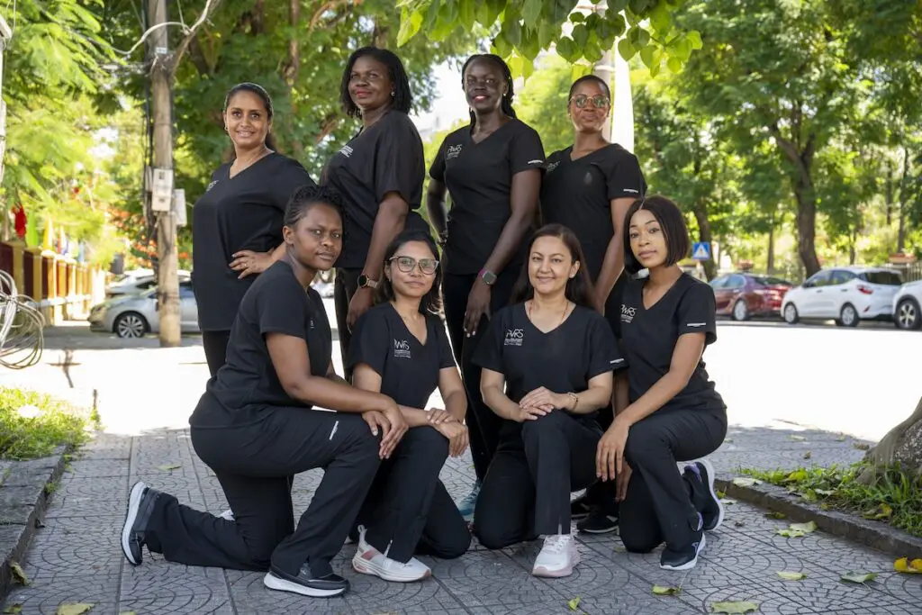 Eight Pioneering Women in Reconstructive Surgery, PWRS, wearing black matching scrub sets pose for a group photo outdoors on a paved sidewalk.