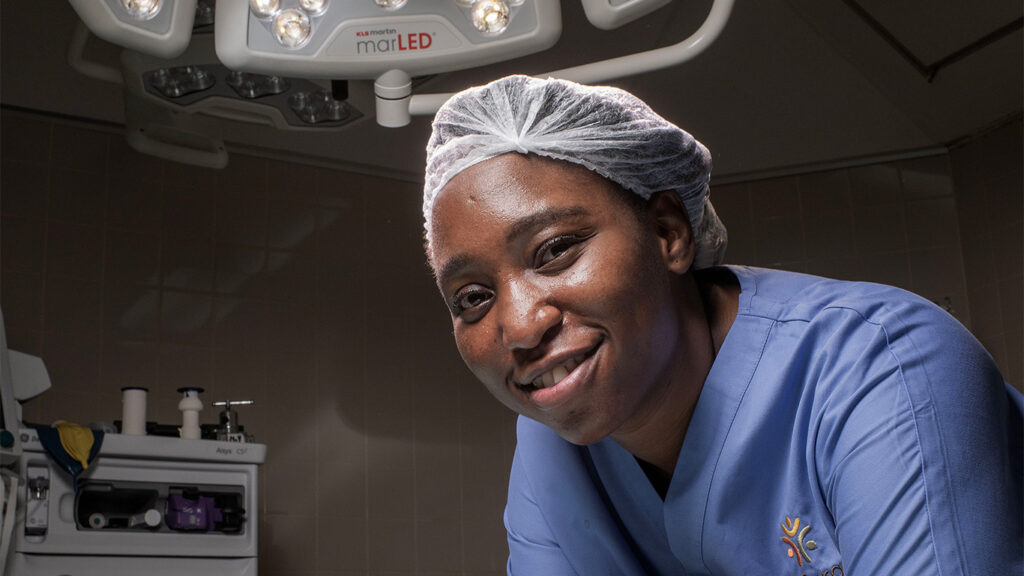 Female Surgeon Leaning on Surgical Table Smiling