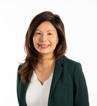 A woman with medium-length brown hair wearing a dark green blazer over a white top, smiling in front of a plain white background.
